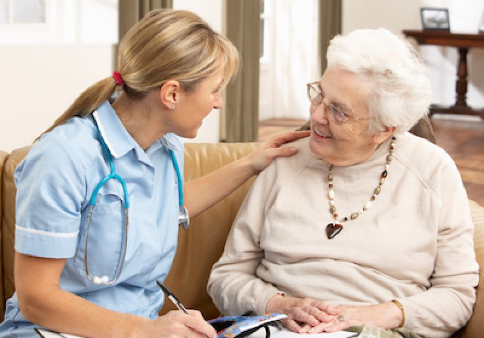 Senior Woman In Discussion With Health Visitor At Home Putting Hand On Shoulder Smiling